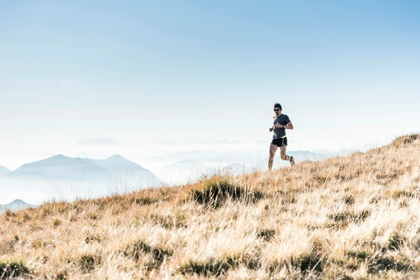 A trail runner crossing a sunlit hillside above the mountains